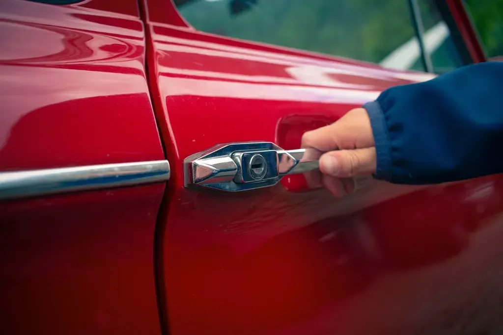 Main ouvrant la portière d'une voiture rouge