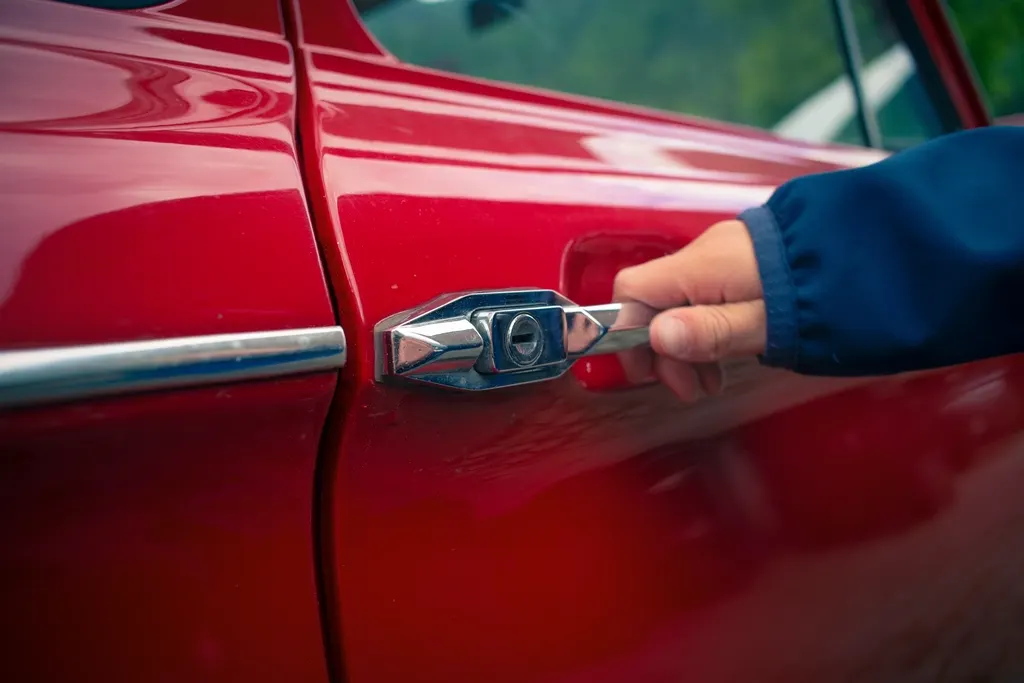 Main ouvrant la portière d'une voiture rouge